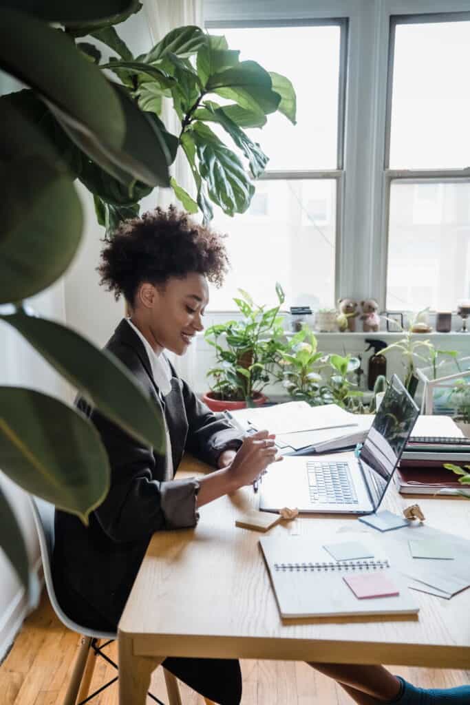 Young woman working on laptop in bright home office with plants.
